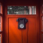 old style corded black phone mounted on red paneled wall