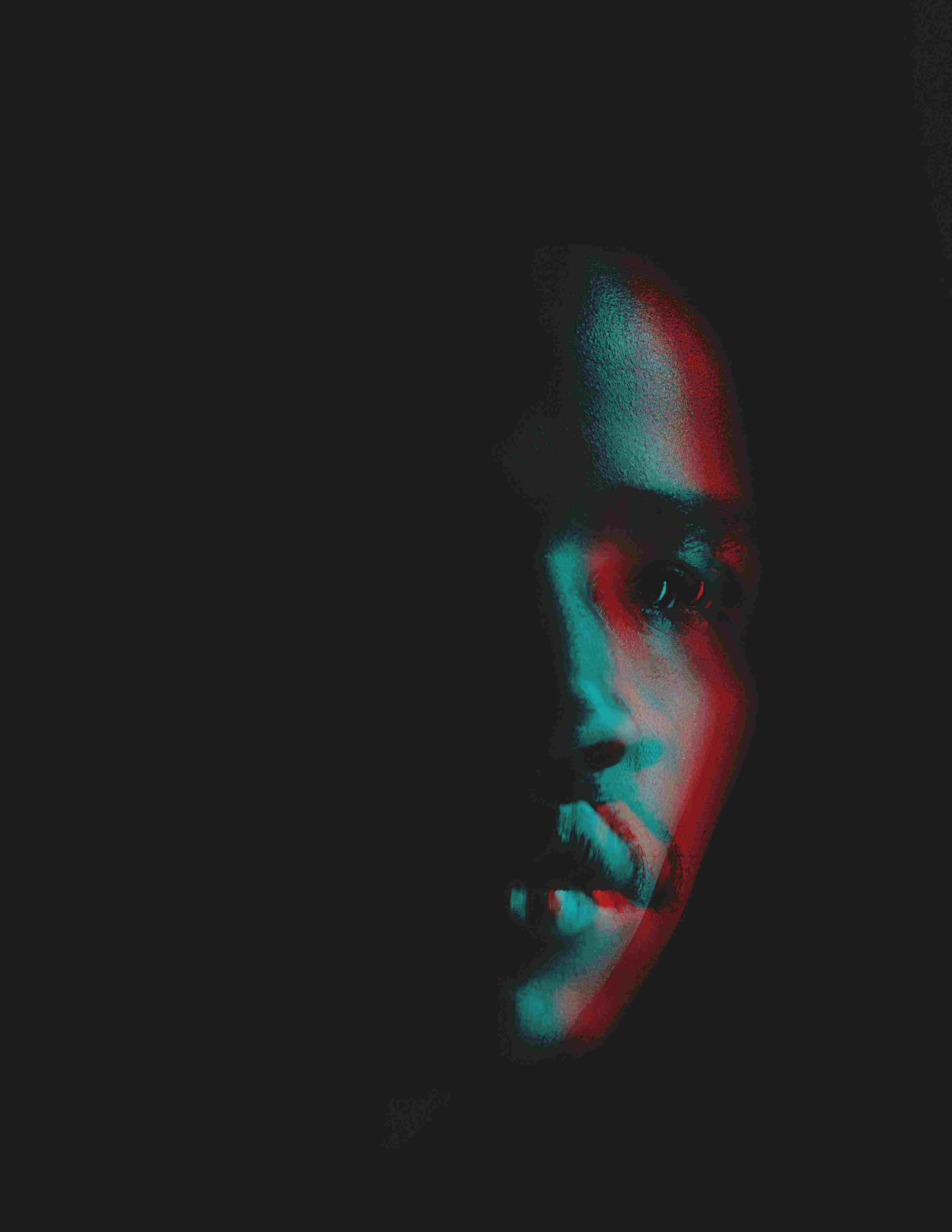 1/3 visible profile view of a Black man's face on a dark background, with a slightly out of focus effect that gives an almost prismatic hue to his skin