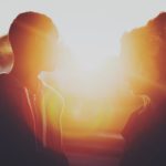 bright sunlight dominates the image from the center and background, with the partially obscured silhouettes of a person on each side, facing each other