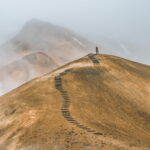 A lone figure, small and far away, steps trailing behind then on a desolate hilltop