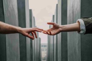 two white hands reaching out between two rows of metal posts to touch