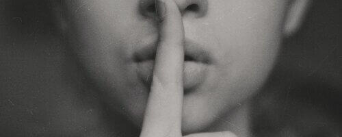 b&W image of woman making a shushing gesture with one finger to her lips