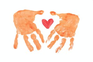 finger-paint style image of two brown hands framing a red heart