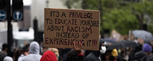 Protester holding a sign for Anti-Racism work that reads: It's a privilege to educate yourself about racism instead of experiencing it