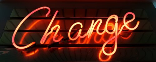 Orange neon lighting spelling the word "Change" in cursive script in front or a mirrored background
