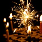 Close-up view of top of a birthday cake in a dark room, focusing on the candles including a sparkler candle