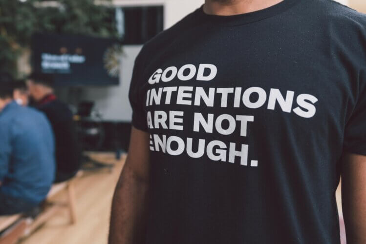 Black man wearing a black T-shirt with white lettering that reads: Good intentions are not enough