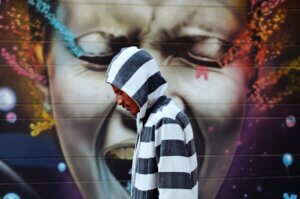 colorful mural of a black woman crying out in anguish, while a black man in a black and white striped hoodie walks past