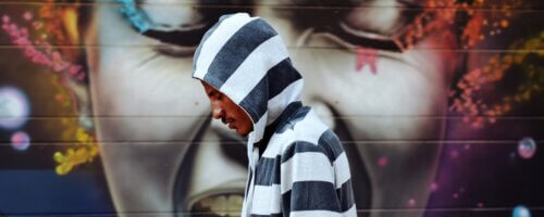 colorful mural of a black woman crying out in anguish, while a black man in a black and white striped hoodie walks past