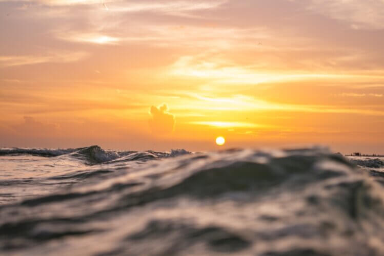 close-up view of waves/tides with sun low on the horizon in the far distance