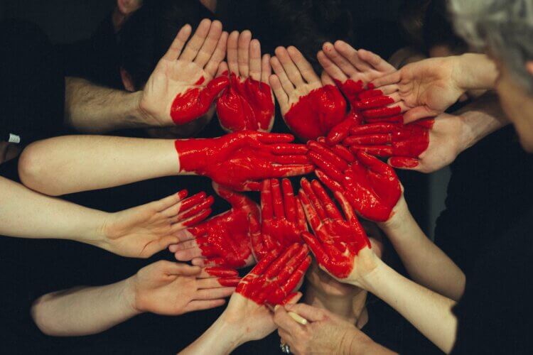 a multitude of white hands palms out, held close to each other with a heart image painted in red across them like they were a canvas