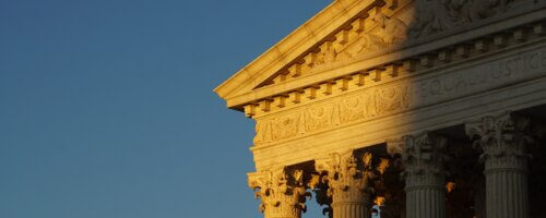 The front façade of the Supreme Court of the United States in Washington, DC, showing just an upper corner, with the portion slight in shadow as it is illuminated gently by the sun