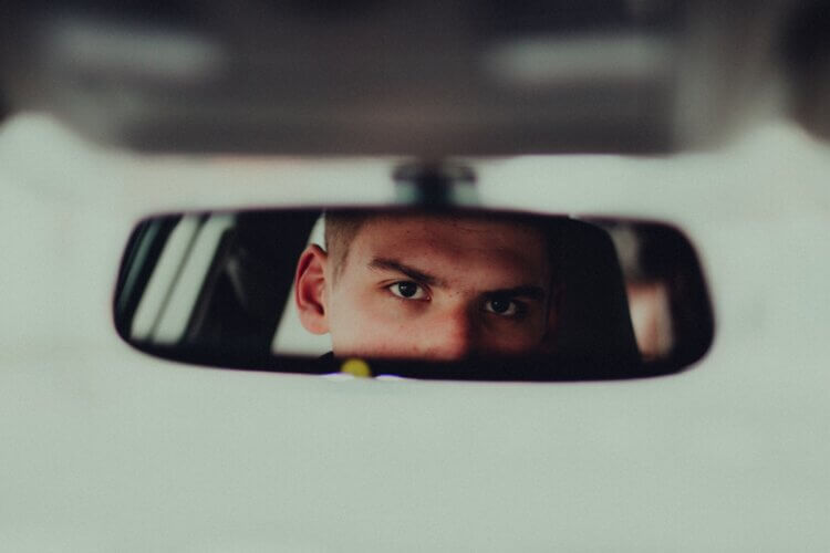 A car rear-view mirror reflecting the eyes and upper face of a man looking intensely ahead