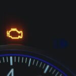 Extreme closeup of a car dashboard, showing an illuminated "check engine" light