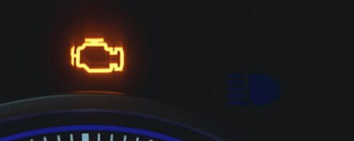 Extreme closeup of a car dashboard, showing an illuminated "check engine" light