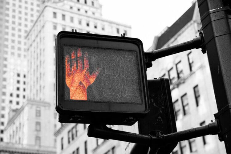 "don't walk" signal displayed, with red hand image looking slightly menacing against a stark city background