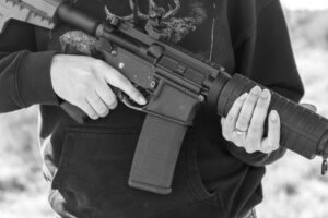 Black and white closeup of a man holding an automatic rifle close to his torso, with face and legs not visible