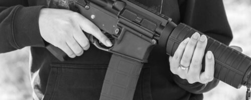 Black and white closeup of a man holding an automatic rifle close to his torso, with face and legs not visible