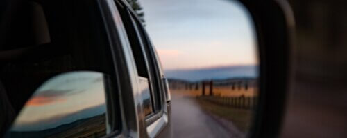 a road and horizon as seen through a side-view mirror of a moving car