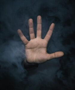 A hand of a white person emerging from a smoky background as if to say, "no farther"