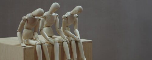 Three wooden marionettes without string (or posable human models for art) sitting on a shelf with heads handing as if weary