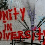 A wall that already had art/graffiti painted on it, also with words in bold red over it reading: Unity in Diversity