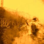 A very heavily yellow-and-orange-toned slightly abstract image of a man doing construction or laboring work near a graffiti-covered low wall