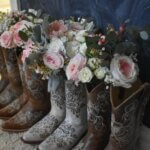 Four pairs of Western-style boots lined up in a row, being used as vases for pretty flowers, mostly pink and white roses