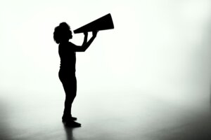 Silhouette of a woman holding a analog megaphone (a large cone used like a bullhorn to amplify voice)