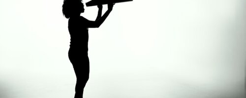 Silhouette of a woman holding a analog megaphone (a large cone used like a bullhorn to amplify voice)