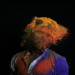 Abstract image of a person in red-and-blue top with face "exploding" a mass of yellow and orange motes