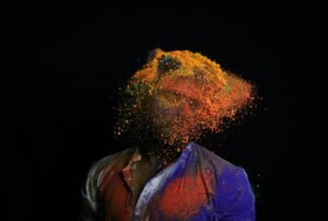 Abstract image of a person in red-and-blue top with face "exploding" a mass of yellow and orange motes