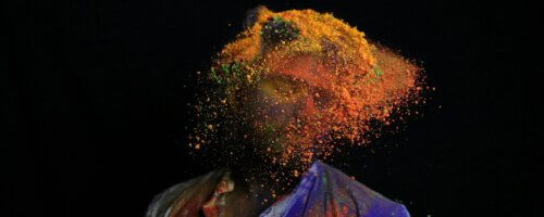 Abstract image of a person in red-and-blue top with face "exploding" a mass of yellow and orange motes