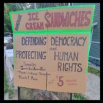 Cardboard sign for a fundraising ice cream sandwich sale that reads, in part: "Homemade Ice Cream Sandwiches" "Defending Democracy and Protecting Human Rights"