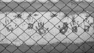 Stark image in black-and-white of handprints on a concrete wall behind a chain-link fence