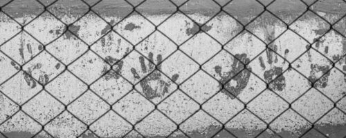 Stark image in black-and-white of handprints on a concrete wall behind a chain-link fence