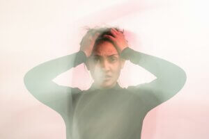 A woman in a moss green shirt holding her hands to her head in confusion, slightly out of focus with a lens flare effect around her