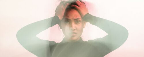 A woman in a moss green shirt holding her hands to her head in confusion, slightly out of focus with a lens flare effect around her
