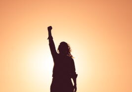 silhouette of woman raising fist in victory backlit by the sun